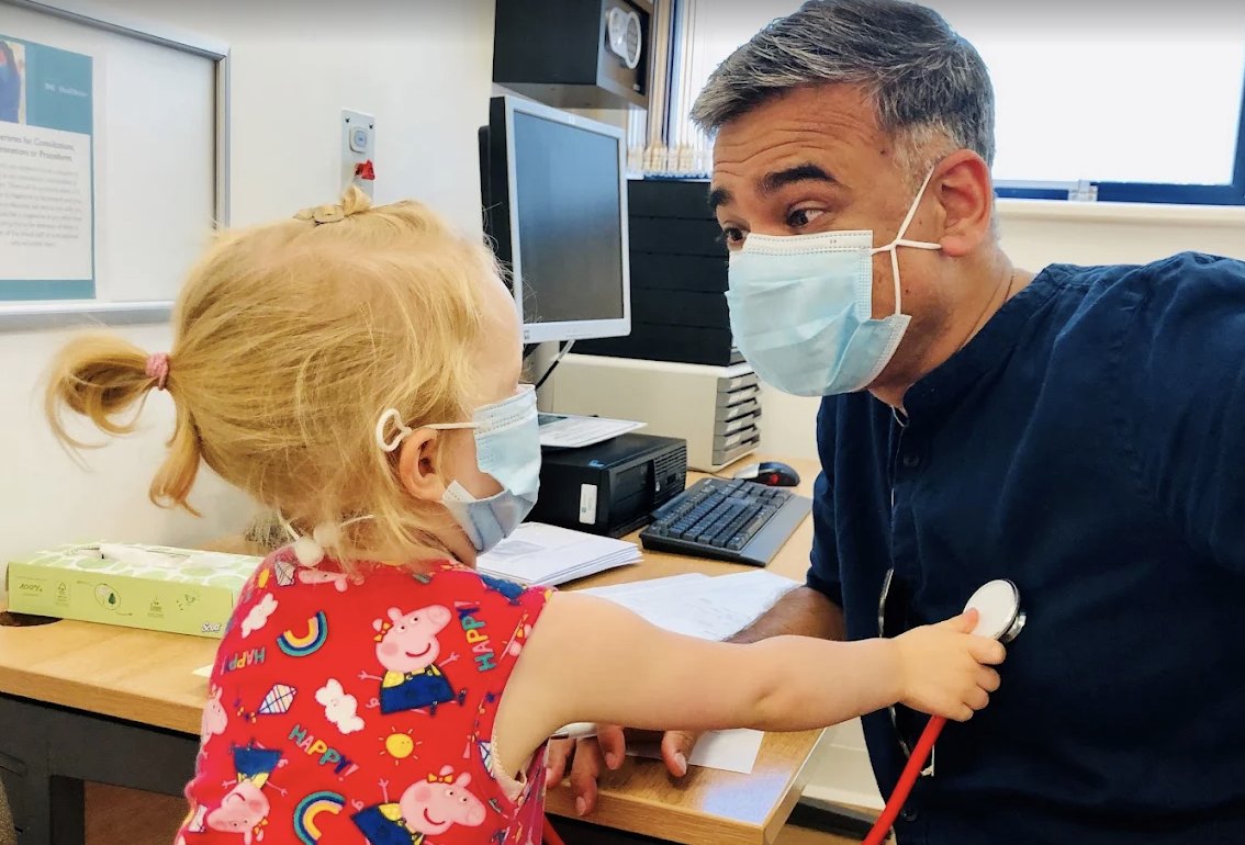 Dr Omi Narayan in clinic, letting a young patient listen to his chest with a stethoscope